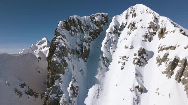 Aerial view tracking a skier on a steep dangerous slope, sunny, winter day