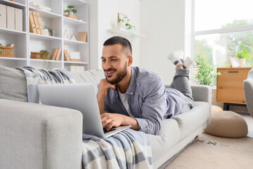 Young man using laptop to search online on sofa at home