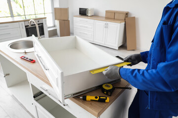 Male worker with ruler assembling drawer in kitchen