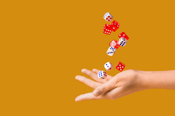 Female hand throwing game dices on orange background