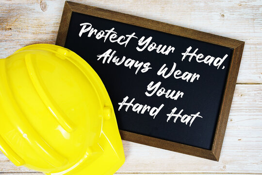 Protect Your Head, Always Wear Your Hard Hat text written on blackboard with safety helmet on wooden background