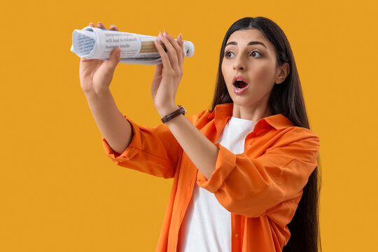 Shocked young woman looking through rolled newspaper on yellow background. Search concept - Powered by Adobe