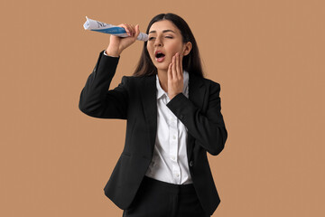 Shocked businesswoman looking through rolled newspaper on beige background. Search concept