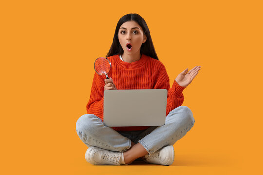 Shocked young woman with magnifier and laptop sitting on yellow background. Search concept - Powered by Adobe