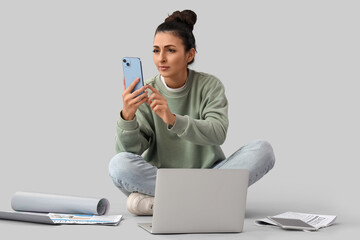 Young woman with laptop using mobile phone on grey background. Search concept