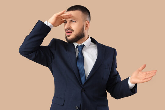 Young businessman looking at something on beige background. Search concept - Powered by Adobe