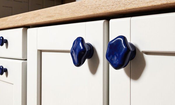 Artisanal Ceramic Hardware. A close-up, macro shot in a kitchen, focusing on the cabinet hardware. The knobs and pulls are