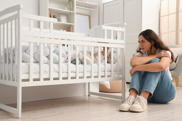 Young mother with her baby in crib suffering from postnatal depression at home