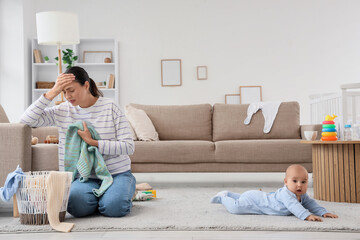 Young mother with laundry and her baby suffering from postnatal depression at home
