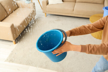 Woman with water dripping from ceiling into plastic bucket in living room