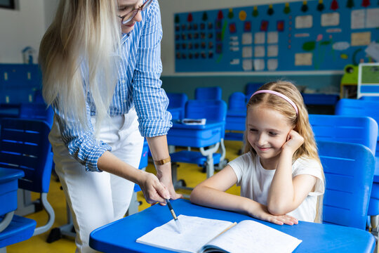 Female teacher helping young girl with schoolwork in classroom