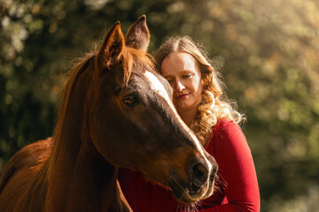 Young woman standing beside a chestnut Arab Lewitzer mix horse, showing closeness and calm connection in soft autumn light.