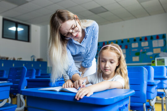 Female teacher helping young girl with writing assignment in classroom