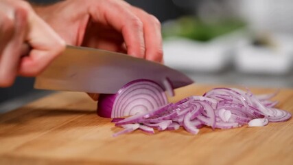 A close-up shot of a person's hand cutting a red onion on a wooden cutting board, capturing the essence of culinary preparation. The sharp knife slices through the onion with precision. Stock Video