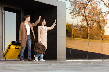 Young couple with luggage waving hands near airport