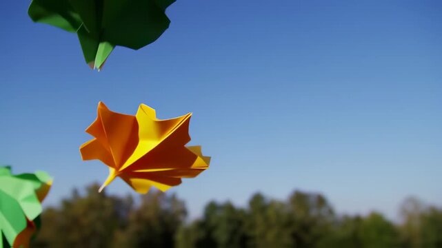 Handmade paper maple leafs with bright colors in the blue sky on a sunny day