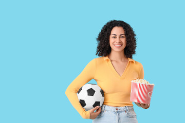 Female African-American sports fan with soccer ball and popcorn on blue background