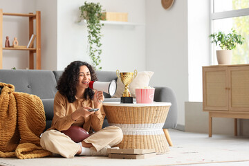 Female African-American sports fan with megaphone watching rugby game at home