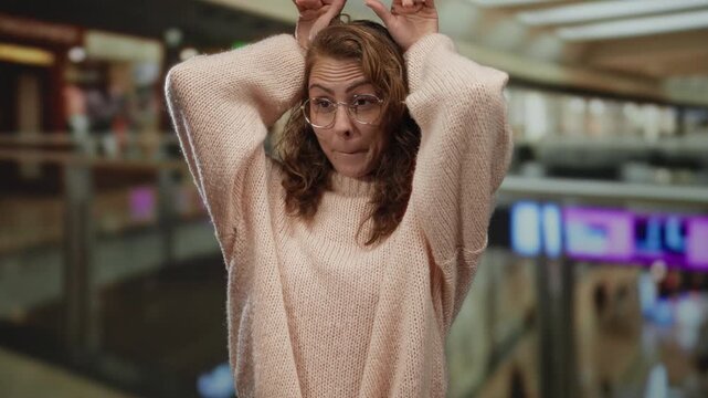 Woman expressing surprise indoors at a mall with her hands on head wearing glasses and a sweater surrounded by indoor shopping center atmosphere and blurred shops.