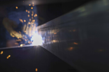 Skilled industrial welder at work, using technology for welding steel. focused job creates intense heat and bright sparks in dark factory, display of powerful metalwork