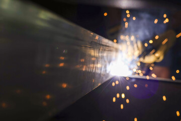 Intense welding process with bright light and hot sparks flying from metal fabrication. skilled worker joining steel beam in dark industrial workshop with focused emotion