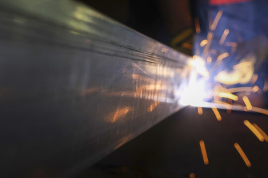 Industrial arc welding close up showing welder at work in factory. Bright, hot sparks fly during metal fabrication on steel beam. Powerful, focused, skilled labor