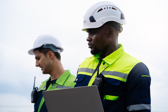 Two men wearing safety gear and helmets are looking at a laptop