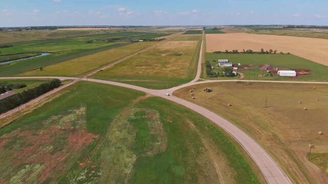 High aerial pan-left following white car on rural North Dakota road amid vast farmland.