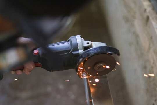 Focused worker using powerful angle grinder to cut metal pipe. Bright sparks fly during industrial cutting process, showing precision and skill in workshop - Powered by Adobe