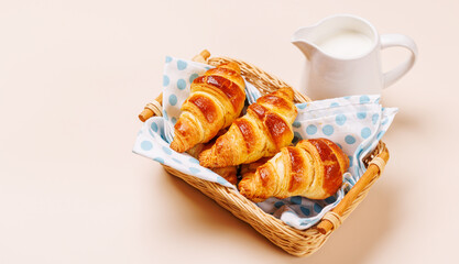Aromatic croissants in wicker basket with milk jug