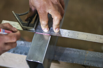 Focused worker hand using ruler and tool for accurate measuring and marking metal beam during...