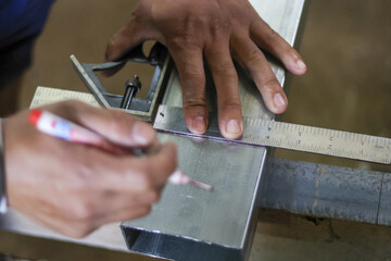 Close up of skilled worker hand with concentration measuring and marking steel tube. Using square ruler tool for precision in metal fabrication workshop