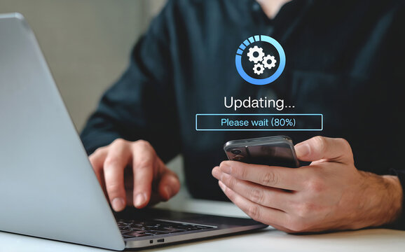 Person updating software on a smartphone while using a laptop, showing a progress bar indicating the update process and a loading icon