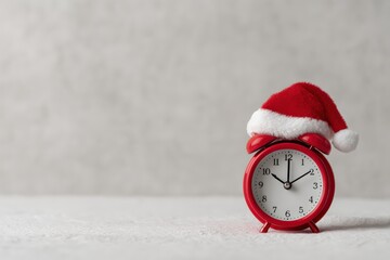 Red alarm clock wearing a Santa hat, signaling holiday time and Christmas countdown on a snowy surface with copy space