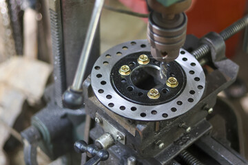 Close up on drill press machine drilling motorcycle disc brake part. Industrial workshop setting...