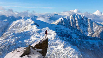 Winter Mountain Climber Standing on Snow-Covered Peak Overlooking Vast Icebound Range Under Clear Blue Sky