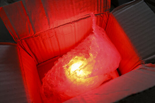 Mysterious glowing object inside cardboard box wrapped in bubble wrap. This surprising package with bright golden light creates an intense red glow from treasure