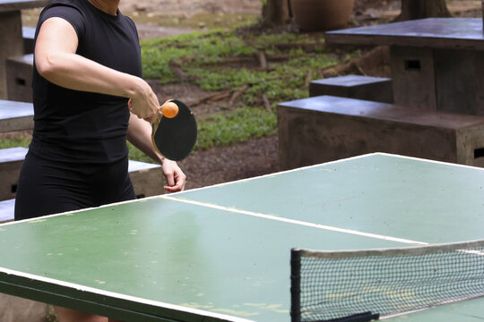 Focused woman playing an active game of table tennis outdoor in park. recreation sport involving paddle, ball, and net for fun, competitive leisure activity