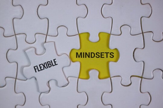 white puzzle with a yellow center piece labeled Mindsets and a white piece labeled Flexible, symbolizing adaptability, positive thinking and collaborative problem solving in teams and personal growth.