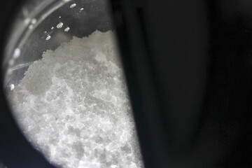 Curious macro view of white crystal powder, possibly salt or another chemical substance seen through microscope. This scientific research reveals detailed mineral texture