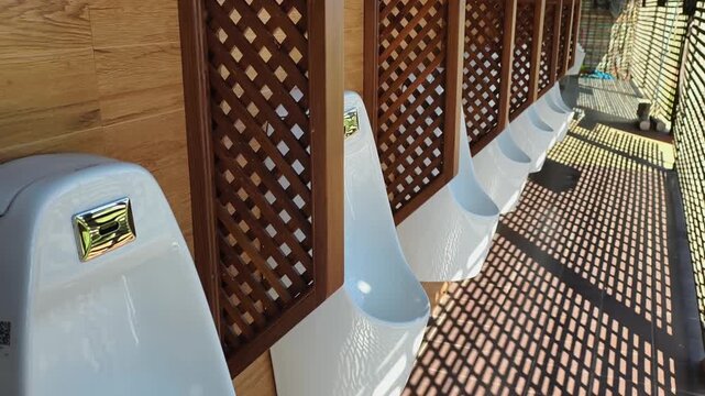 Row of white urinals separated by wooden lattice screens