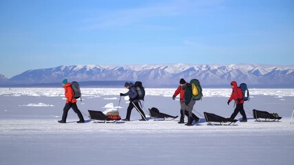 Group of Adventurers trekking across a snow-covered landscape with sleds under a clear blue sky Stock Video