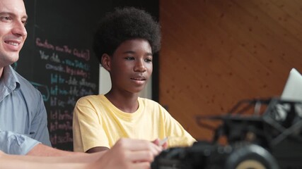 African boy using laptop to program code or prompt with car model placed while teacher and caucasian friend study about robotic construction. Student study about car model structure. Edification