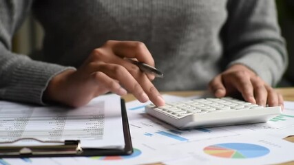 Detailed view of person calculating expenses with calculator and paperwork on desk. Financial data and analysis in a neutral light environment. - Powered by Adobe