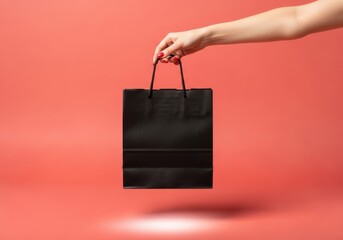 Black shopping bag held by a hand against a vibrant coral background