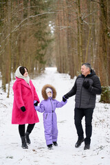 Joyful family walk parents and child stroll along snowy path, holding hands, talking, laughing against backdrop of winter forest landscape. Family moment during winter walk through snowy park, forest.