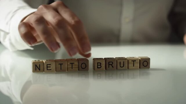 Netto Bruto Block Letters Arrangement on White Background Office Surface. Business Concept. The hand is wearing a white shirt.
