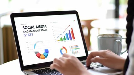 A woman types on a laptop showing social media stats with colorful charts, sitting at a white table with a mug in soft natural light showcasing digital analytics and business strategies. - Powered by Adobe