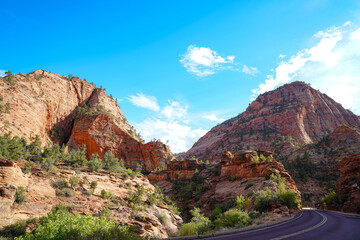 A winding desert road curves between towering red-rock cliffs in Zion National Park, highlighting the rugged formations and vibrant terrain near Angels Landing.