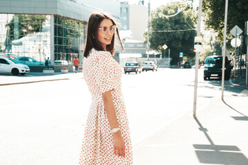 Young beautiful smiling hipster woman in trendy summer dress. Sexy carefree woman posing on the street background at sunset. Positive model outdoors  in sunglasses. Cheerful and happy